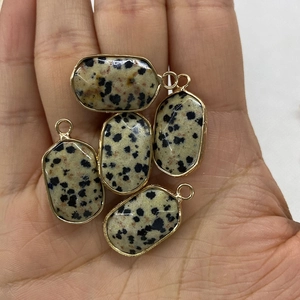 Handheld view of five Dalmatian Jasper oval pendants with gold-plated metal borders