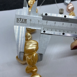 Macro shot of a vernier caliper measuring a 12mm golden baroque tooth-shaped pearl bead