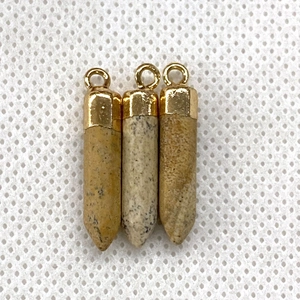 Three bullet-shaped natural stone pendants with golden metal caps and loops on white background