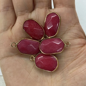 Handheld view of five faceted red natural stone pendants with gold metal edge frames