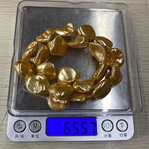 Detailed view of irregular baroque golden pearls weighing 65.57g on a digital scale