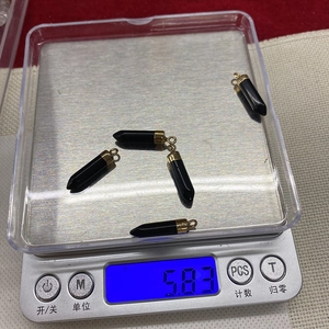 Detailed view of 5 faceted black stone bullet pendants on an electronic scale for weight check