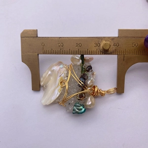 Dettaglio del ciondolo in perla e madreperla con filo dorato, larghezza di circa 42 mm