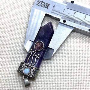 Detail shot of amethyst pendant with vintage floral metal base being measured by caliper