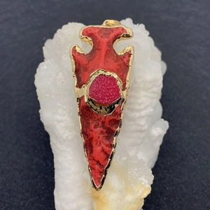 Detalle de colgante de flecha roja con borde bañado en oro e incrustación de druzy