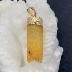 Cylindrical yellow crystal pendant with gold-plated metal cap on a white mineral background