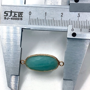 Detail view of faceted oval amazonite stone connector with gold rim being measured by caliper