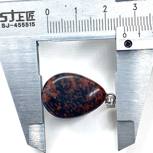 Macro shot of red and black natural stone teardrop pendant measured with calipers