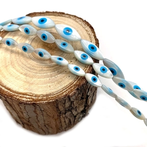 Macro detail of marquise shell beads with evil eye pattern on natural wood stand