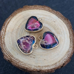 Tre ciondoli a cuore in pietra imperiale con bordo dorato su una superficie di legno naturale
