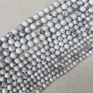Détail de perles en howlite blanche veinée de gris sur fond de toile de jute