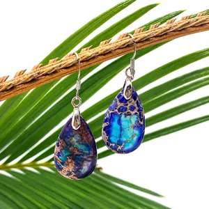 Macro shot of natural teardrop turquoise earrings hanging on wood with palm leaf background