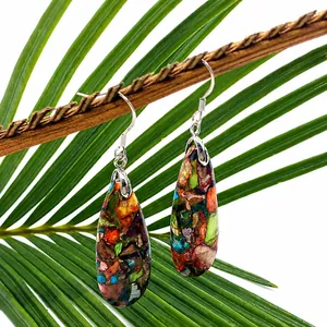 Macro detail of colorful teardrop stone earrings hanging on a green palm leaf