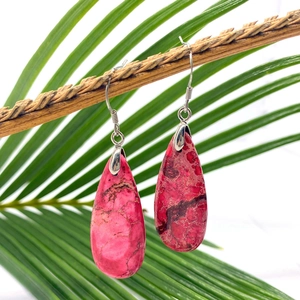 Pink teardrop natural stone earrings with silver hooks hanging on a palm leaf branch