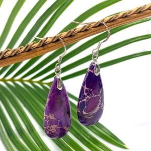 Purple teardrop turquoise earrings with mesh patterns hanging on a natural tree branch