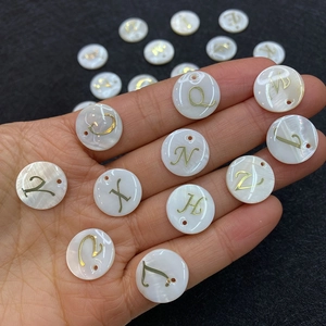 Close-up of 15mm white freshwater shell alphabet charms with gold letters held in hand