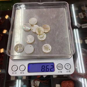 Macro detail of 15mm natural shell pendants with golden letters on electronic scale