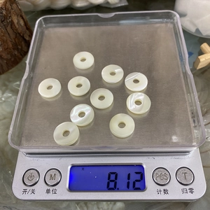 Makroaufnahme von 10 Stück weißen Perlmuttschalen Ringperlen auf einer Digitalwaage