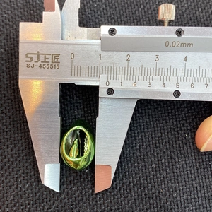Detailed macro view showing a 10mm green polished shell bead measured by a caliper