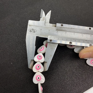 Macro shot showing 12mm heart-shaped shell beads with pink evil eye design on calipers