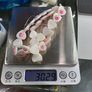 Detailed view of 30.29g weight for heart-shaped evil eye shell beads on a digital scale