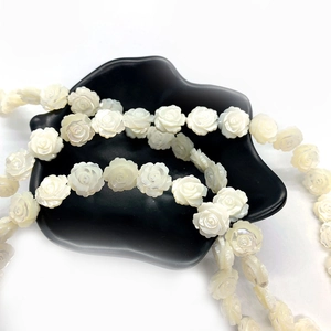 Macro detail of white carved shell rose beads with pearlescent luster in a black bowl