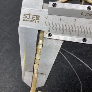 Macro shot of 2mm square natural shell beads being measured with a caliper for DIY jewelry