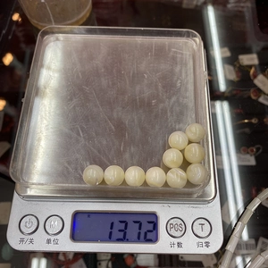 Makroaufnahme von neun cremeweißen Muschelperlen auf einer Digitalwaage mit 13,72g Gewicht