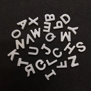 Flat round white mother of pearl alphabet beads for DIY jewelry making on black background