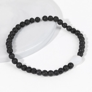 Makro-Detail von schwarzen Lavastein-Perlenarmband mit weißem Herzanhänger auf Tablett