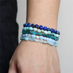 Close-up of five layered natural irregular stone bracelets on a wrist with elastic cords