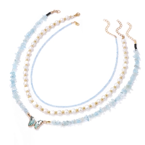 Macro detail of three-layered necklace set featuring blue stone, pearls and butterfly pendant