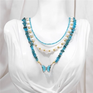 Detailed view of triple-layered necklace with blue stones, pearls and butterfly pendant