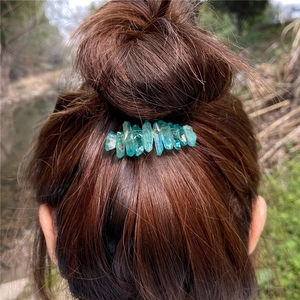 Close-up of light blue raw crystal hair clip worn on a messy bun with natural lighting