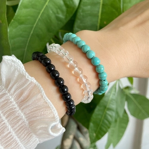 Three beaded bracelets in black, clear, and turquoise on wrist with lace sleeve