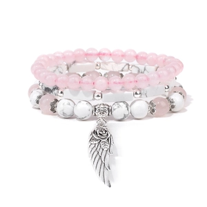 Dettaglio dei bracciali multistrato in marmo bianco con ciondoli rosa e ali