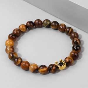 Dettaglio delle perle in occhio di tigre e del ciondolo a ferro di cavallo dorato sul bracciale