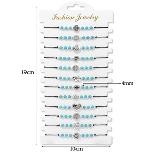 Detailed view of 12 woven bracelets with blue beads and mixed metal charms on a white card