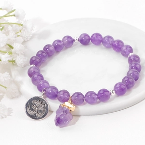 Detail eines Amethyst-Perlenarmbands mit Om-Anhänger und Naturstein auf Marmorsockel