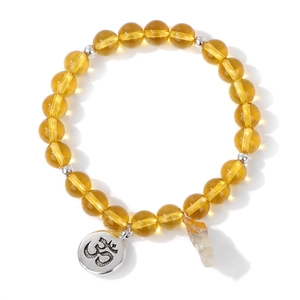 Detail eines Bernstein-Perlenarmbands mit Om-Symbol-Anhänger und Rohkristall-Charm auf Weiß