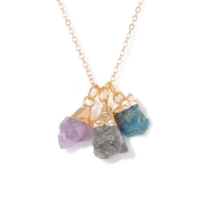 Detailweergave van drie natuurlijke ruwe stenen aan een gouden ketting met paarse hangers