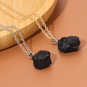Dettaglio di pendenti in pietra naturale nera irregolare su catene sottili oro e argento