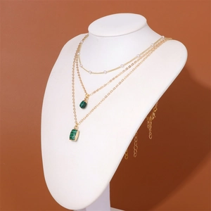 Detailed close-up of triple-layered 18k gold chain necklace with green stone and pearls