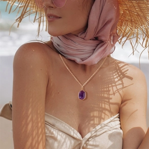 Collana a catena d'oro con ciondolo di ametista viola indossata al sole in spiaggia