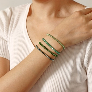 Detail von vier geschichteten Perlenarmbändern in Grün- und Blautönen an einem Handgelenk