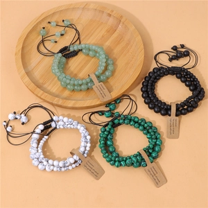 Detail of four natural stone beaded bracelets in green, black, and marble white with adjustable cords