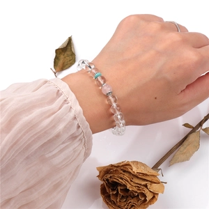 Detalle de pulsera de cuentas de cristal blanco con cuenta rosa y amuletos plateados