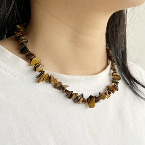 Détail d'un collier en perles de pierre d'œil de tigre irrégulières sur un t-shirt blanc