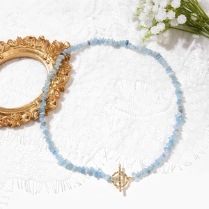 Pale blue gemstone gravel necklace with a golden OT buckle on white lace background