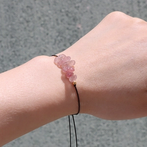 Detail van handgemaakte armband met roze stenen, zwart koord en gouden kraal